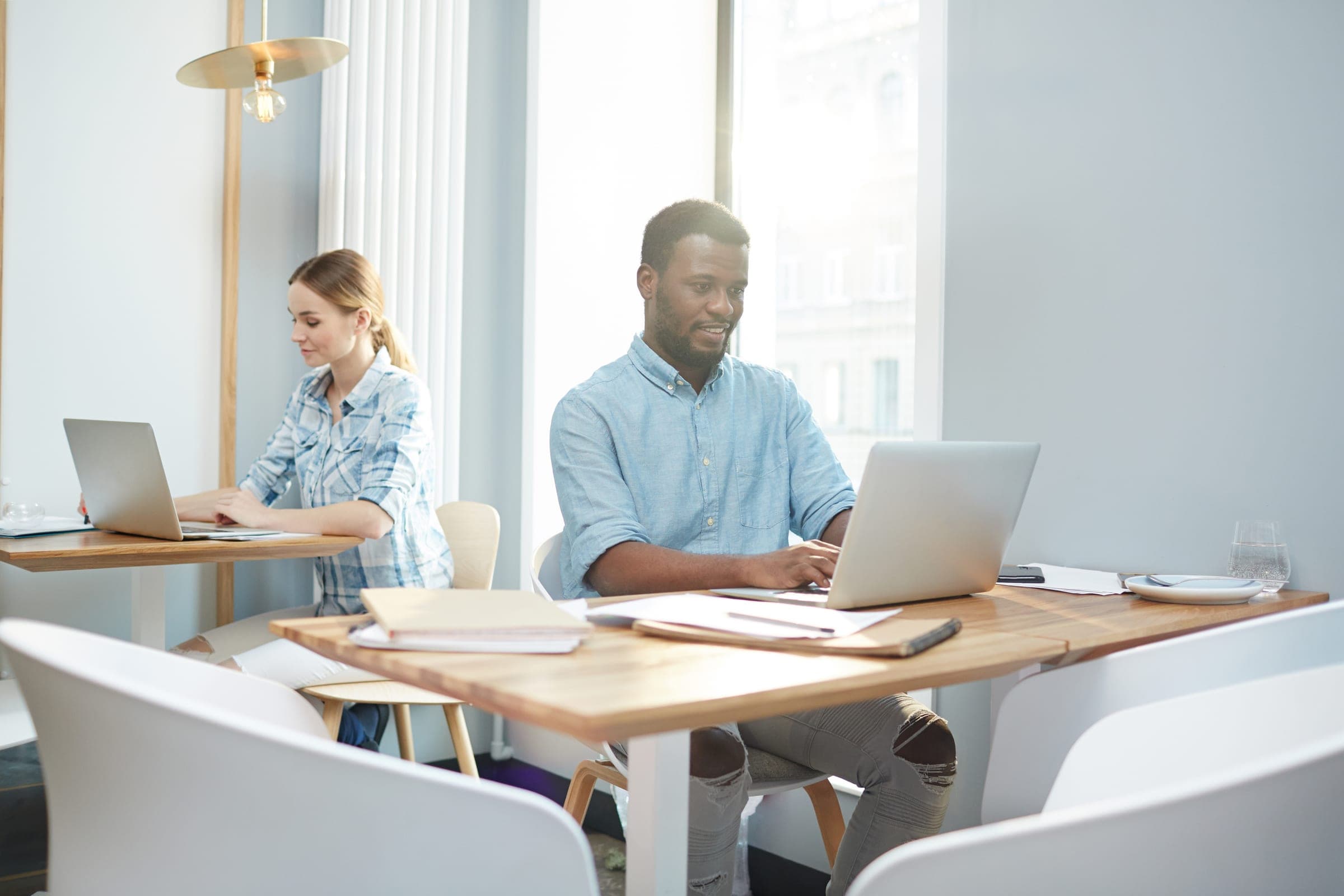 Two colleagues working at laptops in a bright shared workspace
